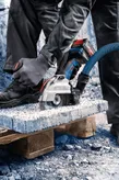 Een persoon met veiligheidsuitrusting zaagt beton met een snoerloze haakse slijper.