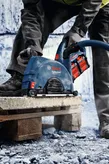 Een persoon die veiligheidsuitrusting draagt, gebruikt een snoerloos gereedschap met stofafzuiging op een stenen plaat.