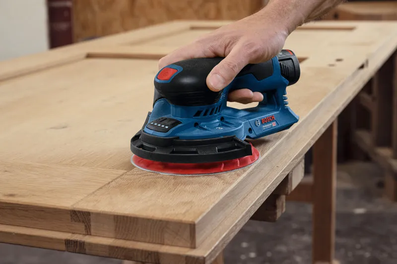 Een persoon schuurt een houten kastdeur met behulp van een snoerloze excentrische schuurmachine.