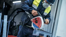 Een persoon die veiligheidsuitrusting draagt, zaagt een metalen balk door met een cirkelzaag.