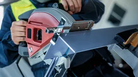 Een persoon die veiligheidsuitrusting draagt, zaagt een metalen balk door met een cirkelzaag.
