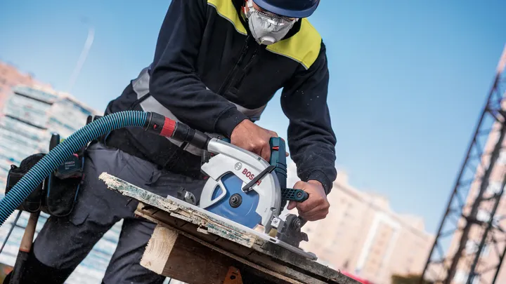 Een persoon die veiligheidsuitrusting draagt, gebruikt een cirkelzaag om hout te zagen op een bouwplaats.