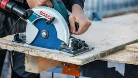 Persoon bedient een cirkelzaag om een houten plank op een werkbank te zagen.