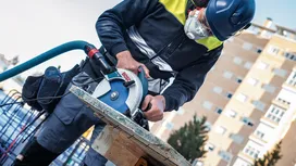 Een persoon met veiligheidsuitrusting zaagt hout met een cirkelzaag op een bouwplaats.