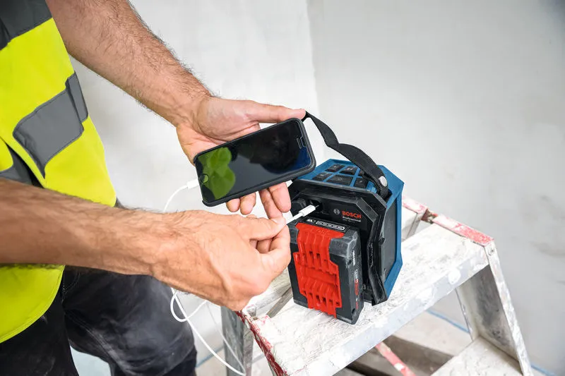 Een persoon die veiligheidsuitrusting draagt, laadt zijn telefoon op met een draagbare powerbank terwijl hij op een ladder staat.