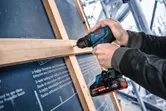 Met een accuboormachine bevestigt iemand binnenshuis hout aan een frame.