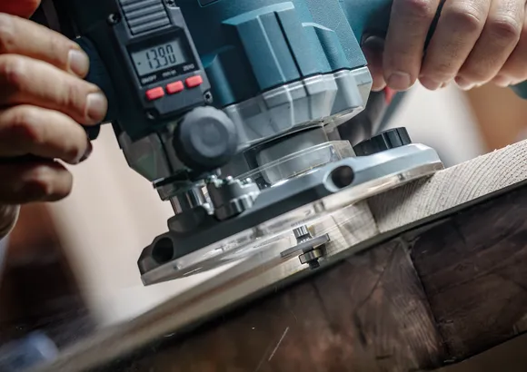 Persoon gebruikt een elektrische freesmachine om de rand van een houten plank vorm te geven.