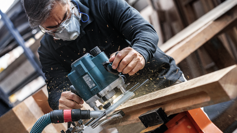 Een persoon met veiligheidsuitrusting bewerkt hout met een bovenfrees.