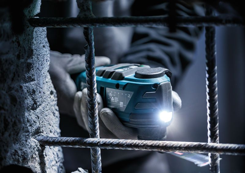 Een persoon die veiligheidsuitrusting draagt, gebruikt een snoerloze multi-cutter met een led-lampje in de buurt van wapeningsstaal.