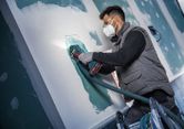 Een persoon die veiligheidsuitrusting draagt, gebruikt een snoerloze multi-cutter om gipsplaat te snijden.