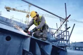 Een persoon met veiligheidsuitrusting slijpt metalen balken met een draadloze haakse slijper.