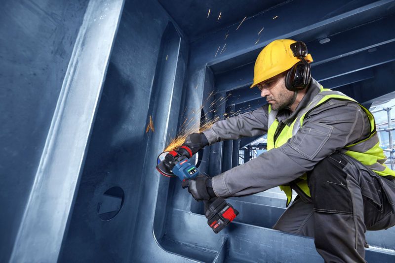 Een persoon met veiligheidsuitrusting maalt metaal in een grote stalen constructie.