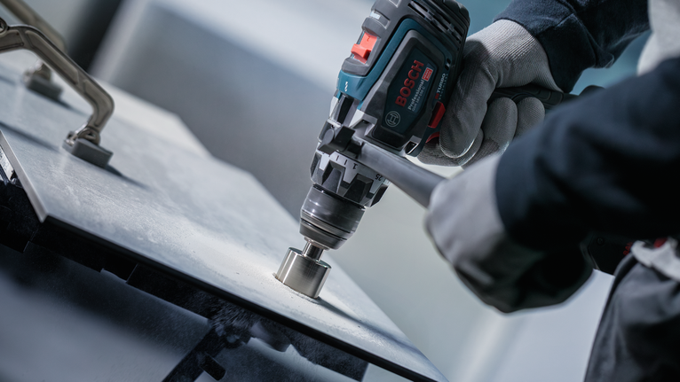 Een persoon met veiligheidsuitrusting boort een gat in een metalen plaat.