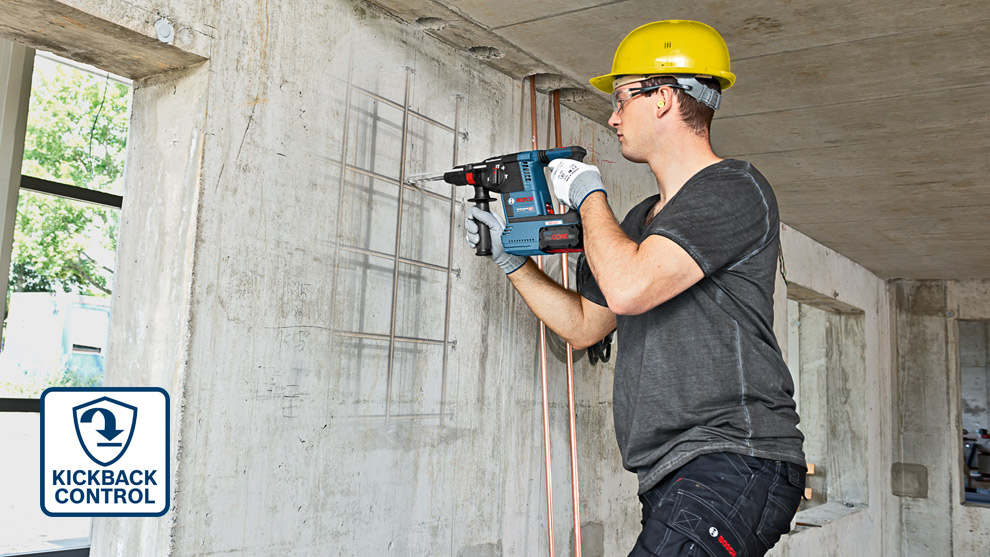 En mann med hjelm bruker en blå Bosch Professional bor på betongvegg.