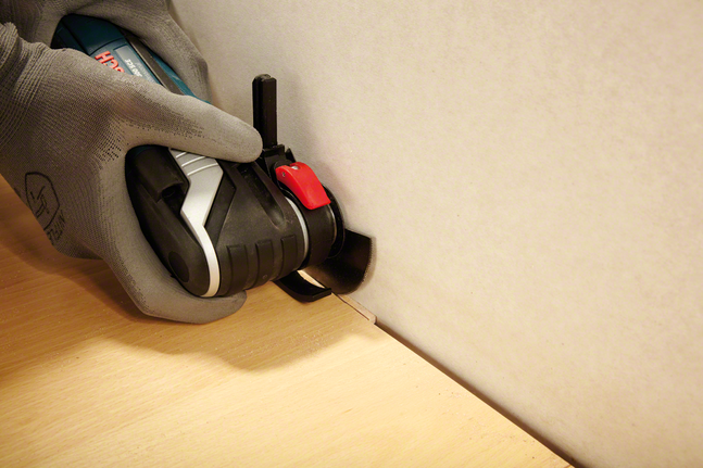 En person med sikkerhetsutstyr skjærer i treverk ved kanten av en vegg med et elektroverktøy.