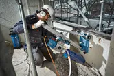 En person med sikkerhetsutstyr bruker et borestativ til å bore et hull i en betongvegg.