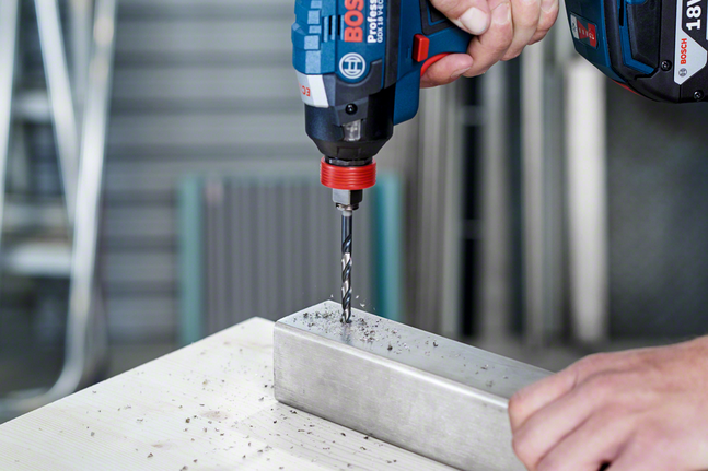 En person borer i en metallbjelke med en batteridrevet drill.