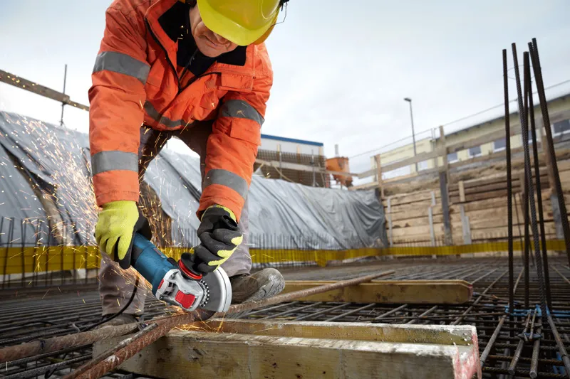 Arbeider med sikkerhetsutstyr sliper metallarmeringsjern på en byggeplass.