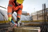Arbeider med sikkerhetsutstyr sliper metallarmeringsjern på en byggeplass.