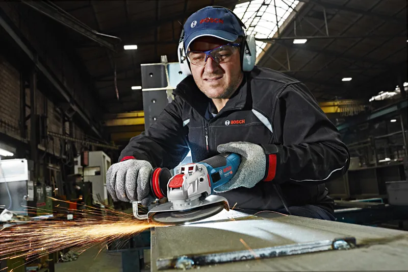 En person med sikkerhetsutstyr sliper metall med en vinkelsliper, og gnister flyr.