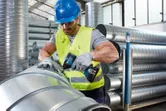 En person med sikkerhetsutstyr fester metallkanaler med et trådløst elektroverktøy.