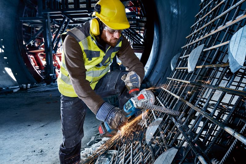 En person som bruker sikkerhetsutstyr bruker en batteridrevet vinkelsliper til å kutte armeringsjern.