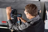 En person med sikkerhetsutstyr borer inn i en skapramme med en elektrisk drill.