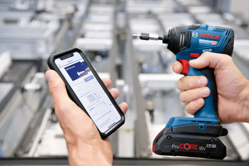 Person som holder en smarttelefon som viser en app ved siden av en trådløs drill.