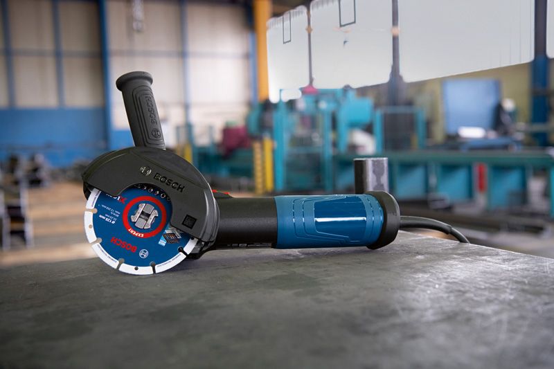 Vinkelsliper med X-LOCK-system hviler på en metallarbeidbenk i et verksted.