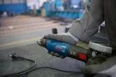 En person med sikkerhetsutstyr holder en vinkelsliper på en metallbenk.