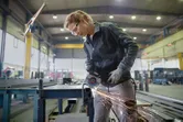 En person med sikkerhetsutstyr sliper metall på en arbeidsbenk, noe som produserer gnister.