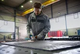 En person med sikkerhetsutstyr sliper en metalloverflate, noe som skaper gnister i et verksted.
