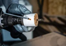En person med sikkerhetsutstyr bruker en boremaskin med hullsag til å skjære gjennom tre.
