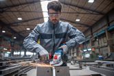 En person med sikkerhetsutstyr sliper metall med en batteridrevet vinkelsliper i en fabrikk.