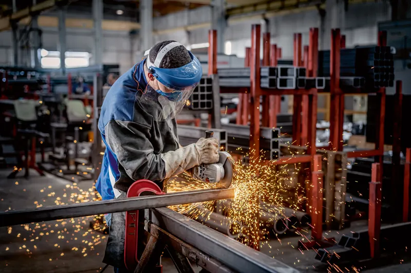 En person som bruker sikkerhetsutstyr bruker en vinkelsliper til å skjære metall, noe som produserer gnister.