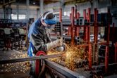En person som bruker sikkerhetsutstyr bruker en vinkelsliper til å skjære metall, noe som skaper gnister.
