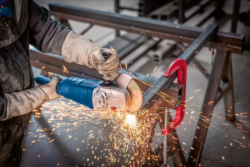 En person med sikkerhetsutstyr sliper metall, og produserer gnister med en vinkelsliper.