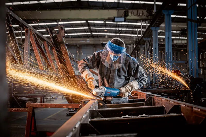 En person med sikkerhetsutstyr sliper metall, noe som produserer sterke gnister i en fabrikk.