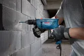 En person med sikkerhetsutstyr borer inn i en betongblokkvegg med en slagbormaskin.