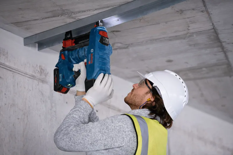 En person med sikkerhetsutstyr fester en metallkanal til et betongtak med en batteridrevet betongspikerpistol.
