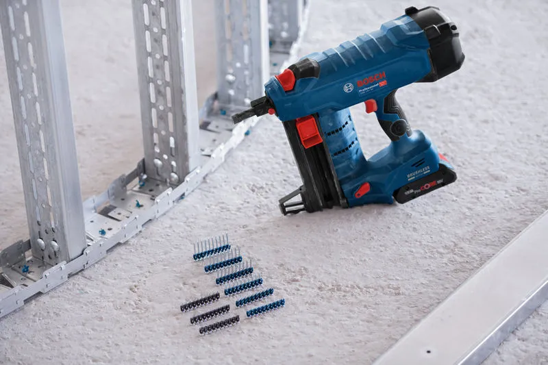Batteridrevet spikerpistol plassert på gulvet ved siden av festelister og metallstendere til rammen.