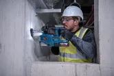 En person med sikkerhetsutstyr borer inn i en betongvegg med en borhammer.