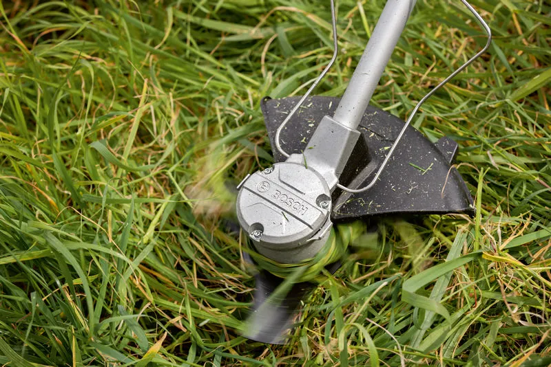 Batteridrevet rydder trimmer høyt gress med roterende blad.