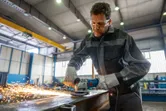 En person med sikkerhetsutstyr sliper metall, noe som produserer gnister i et industriverksted.