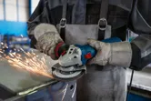 En person med sikkerhetsutstyr sliper metall med en vinkelsliper, og gnister flyr.