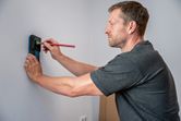 Person som markerer en vegg med blyant mens han bruker en elektronisk detektor.