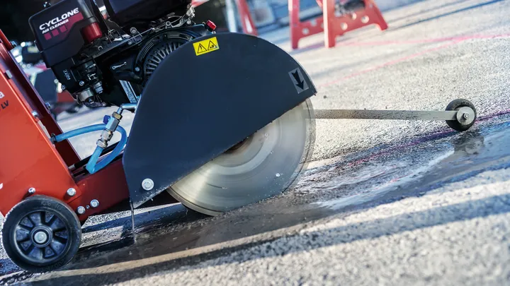 Betongsag skjærer vått fortau på en byggeplass.