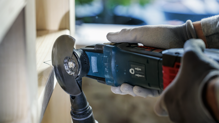 Person med sikkerhetsutstyr som bruker et elektroverktøy til å skjære i tre.