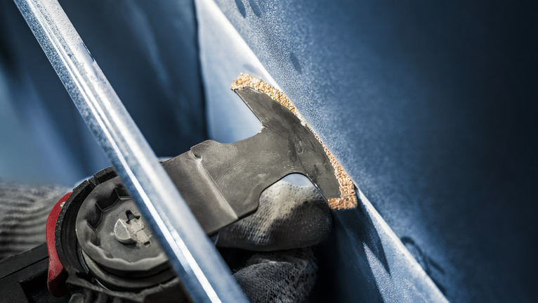 En person som bruker sikkerhetsutstyr bruker et oscillerende verktøy til å skjære et panel.