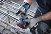 En person med sikkerhetsutstyr holder en batteridrevet slagtrekker mens han kneler på en metallrist.